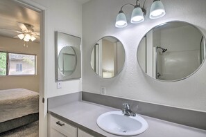 Un baño con un lavamanos blanco, dos espejos redondos y un ventilador de techo.