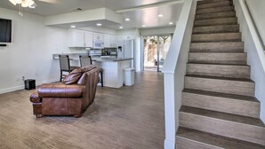 Amplia sala de estar con un sofá de cuero marrón, una cocina con gabinetes blancos y una escalera de madera.