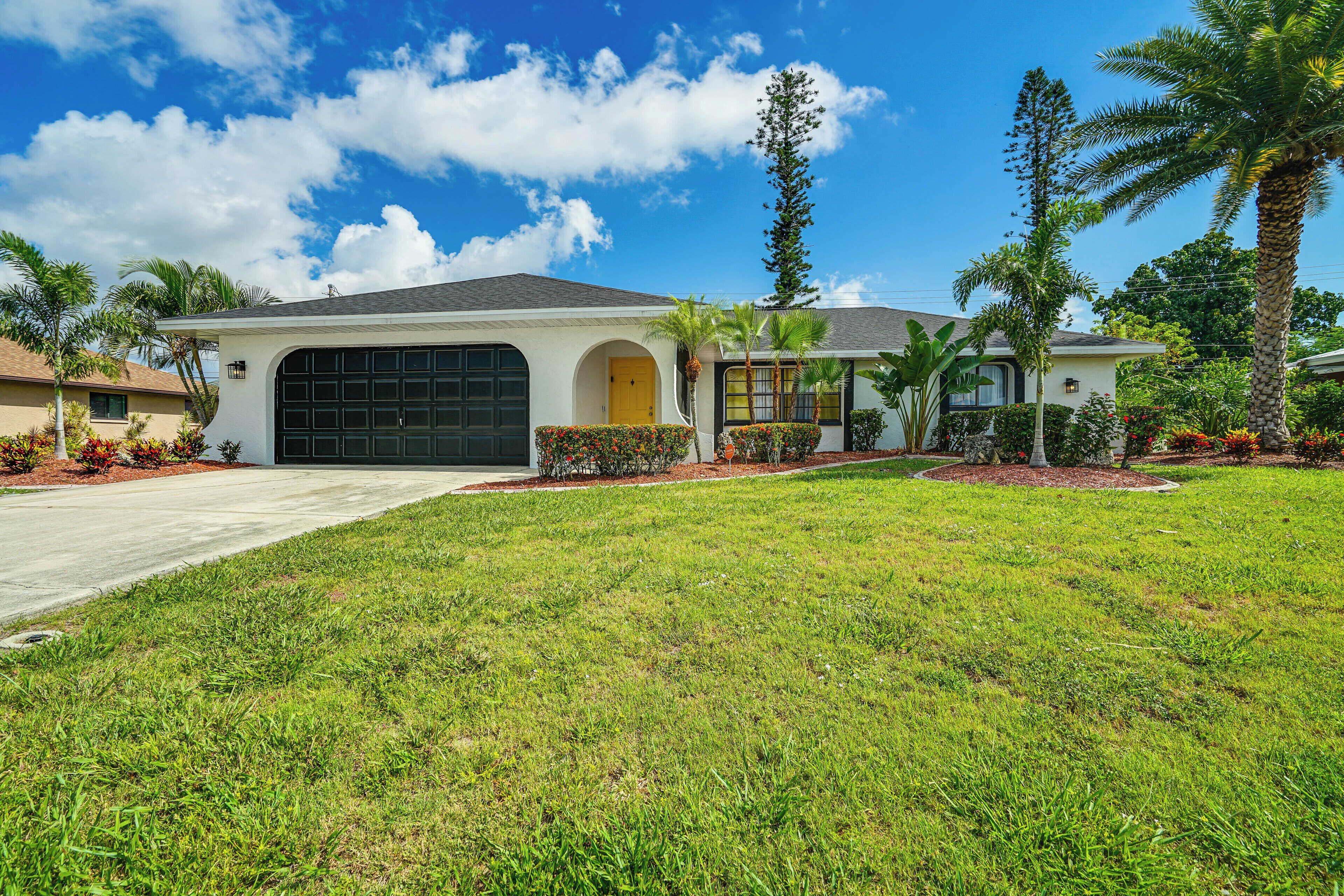 A residential house with a garage, a well-maintained lawn, and tropical landscaping.
