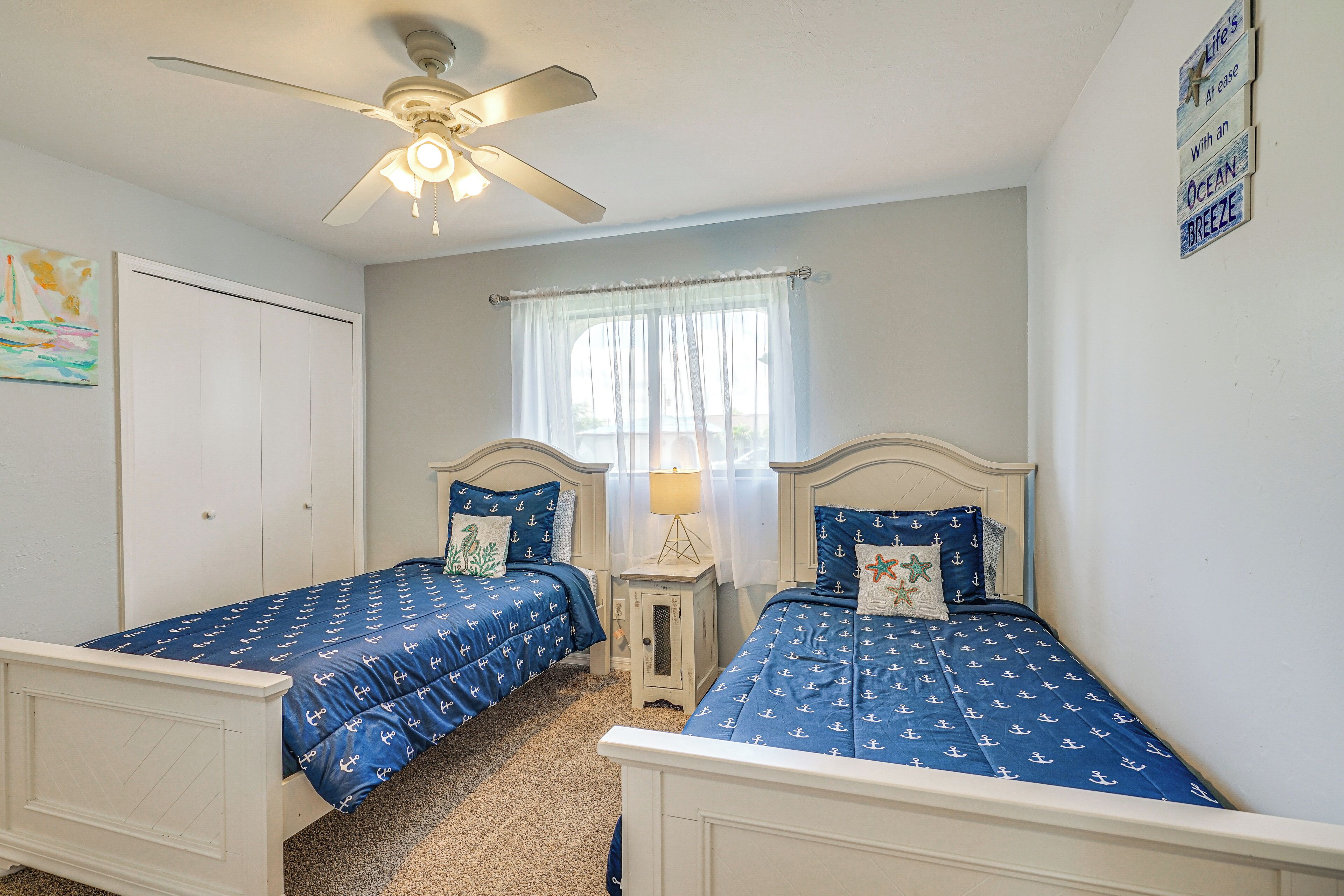 A bedroom with two beds, a ceiling fan, a window with sheer curtains, and a wall with a sign.