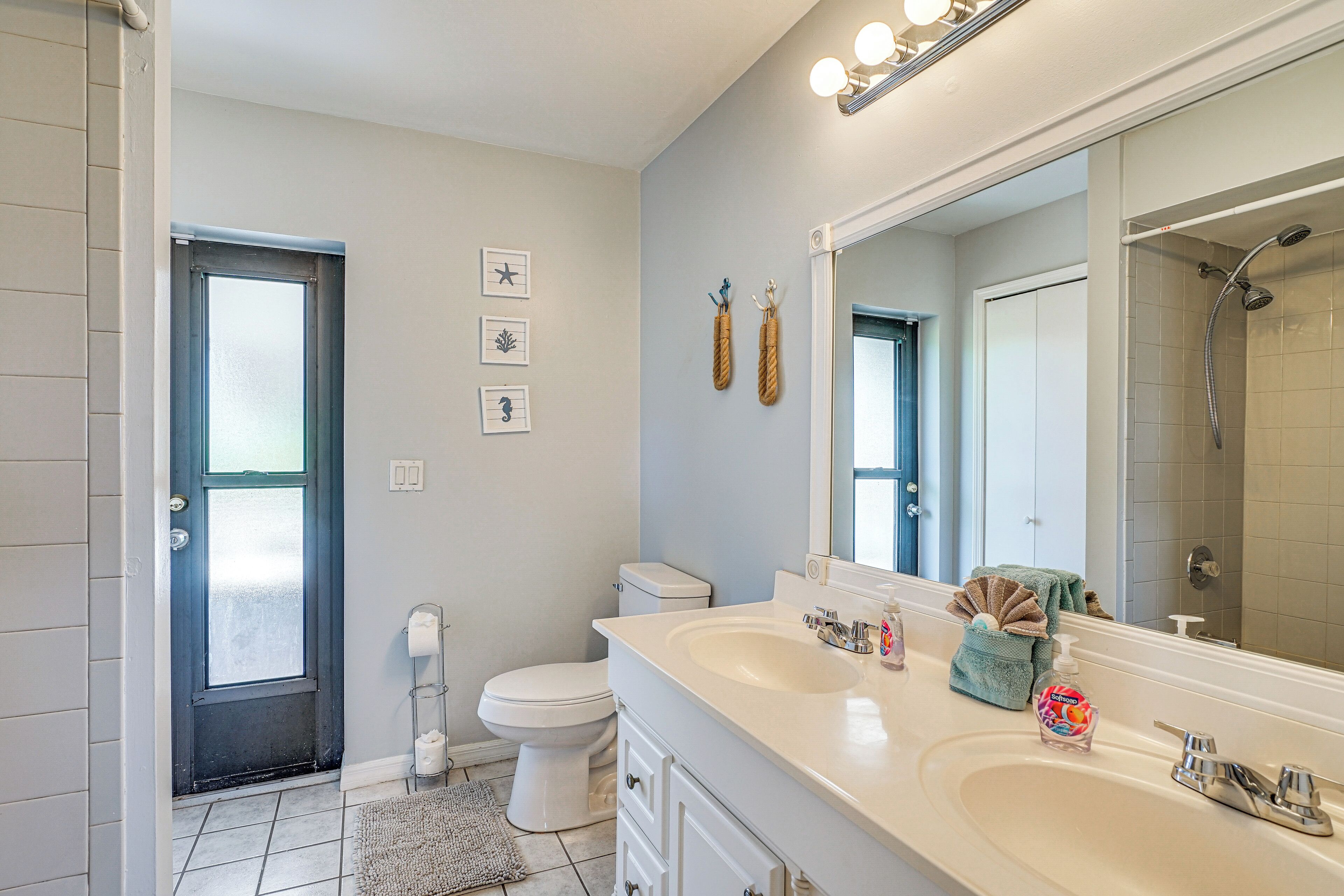 Een badkamer met een witte wastafel, toilet en douche. Er hangen afbeeldingen in lijsten aan de muur en een handdoekrek met handdoeken.