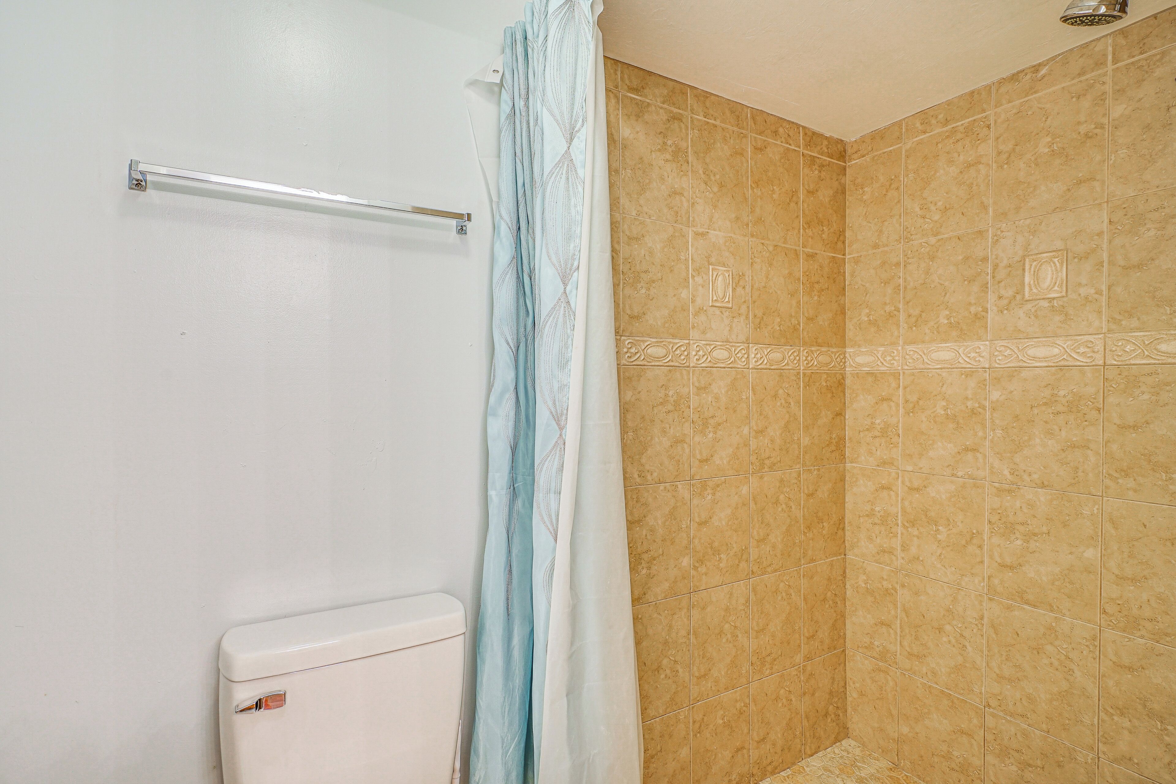 A bathroom with a shower, beige tiled walls, and a white toilet.