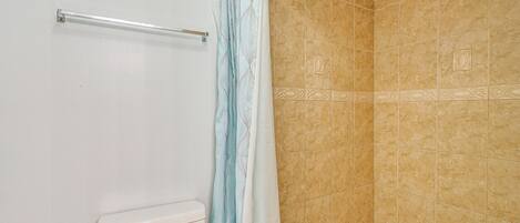 A bathroom with a shower, beige tiled walls, and a white toilet.