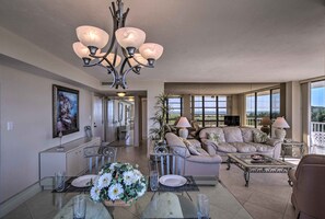 A spacious living room with a dining area, a chandelier, a sofa set, and large windows offering a view. - Sunny Getaway: Community Amenities, Walk to Beach! (Marco Island)