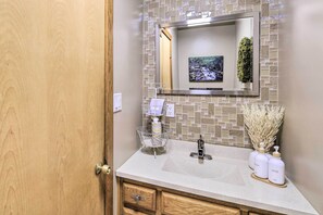 Une salle de bain avec une porte en bois, un pare-feu en carrelage, un lavabo avec un miroir et des articles de toilette posés sur le comptoir.