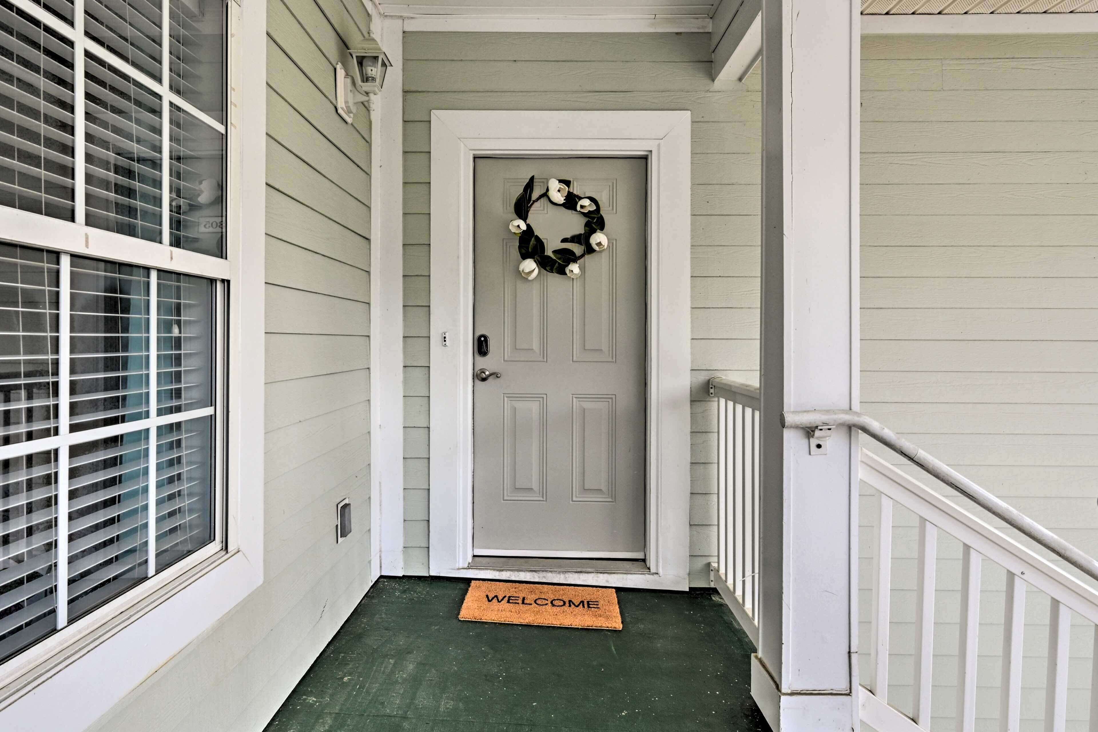 A front door with a wreath, a welcome mat, and a window with blinds.
