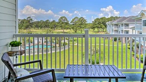 Un balcon avec vue sur un terrain de golf, une piscine et un immeuble à plusieurs étages.