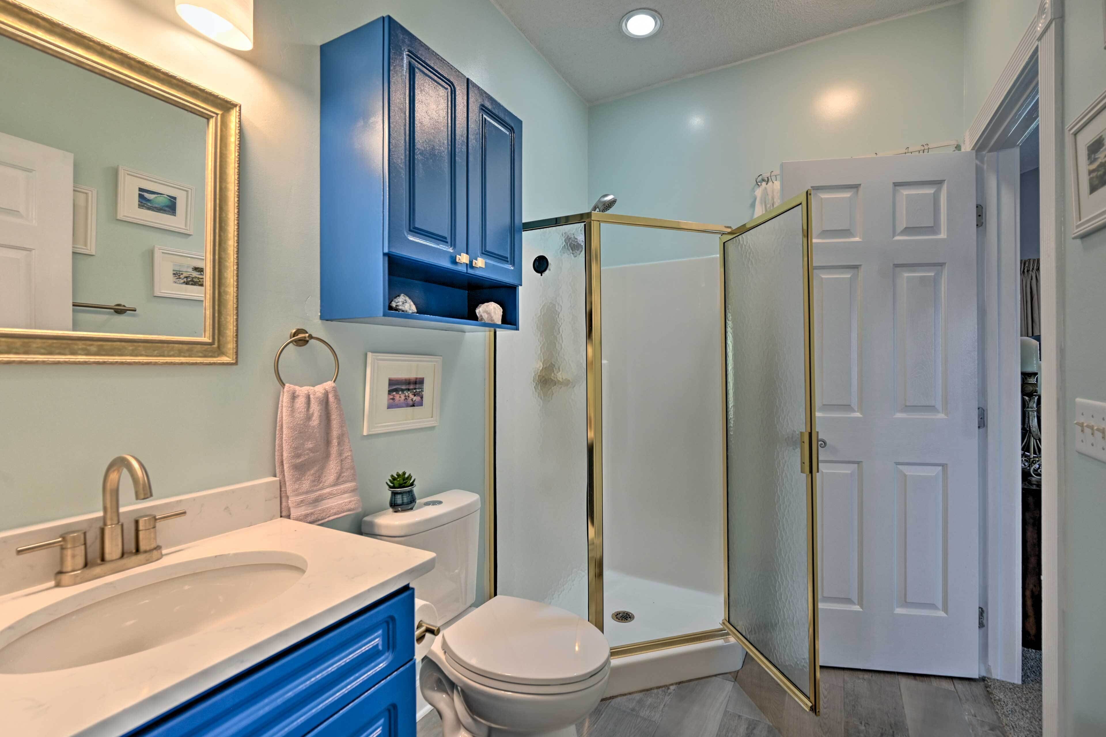 A bathroom with a white sink, blue cabinets, a white toilet, and a glass-enclosed shower.