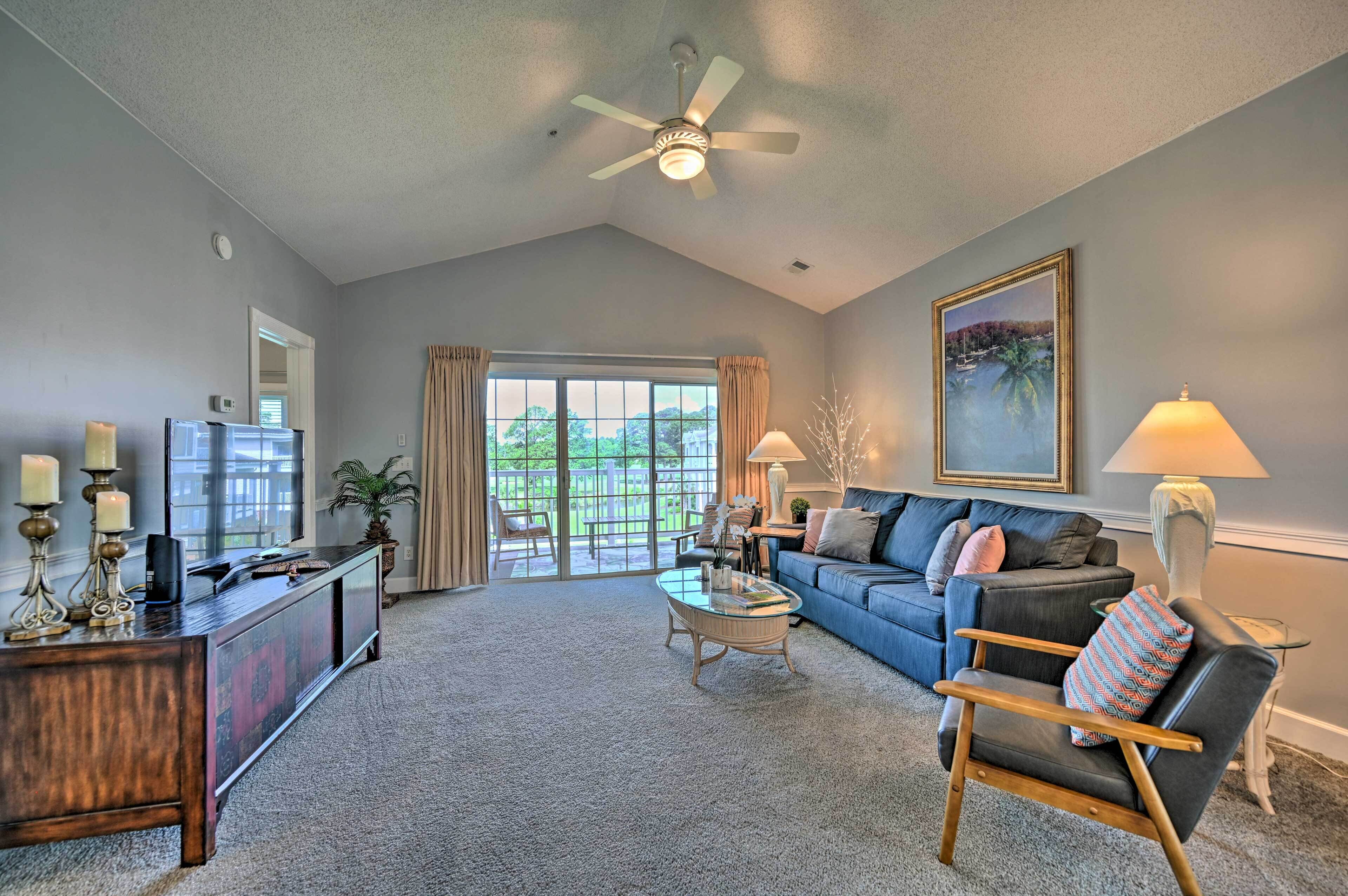 A spacious living room with a large window, a ceiling fan, a sofa, a coffee table, and a TV on a wooden cabinet.