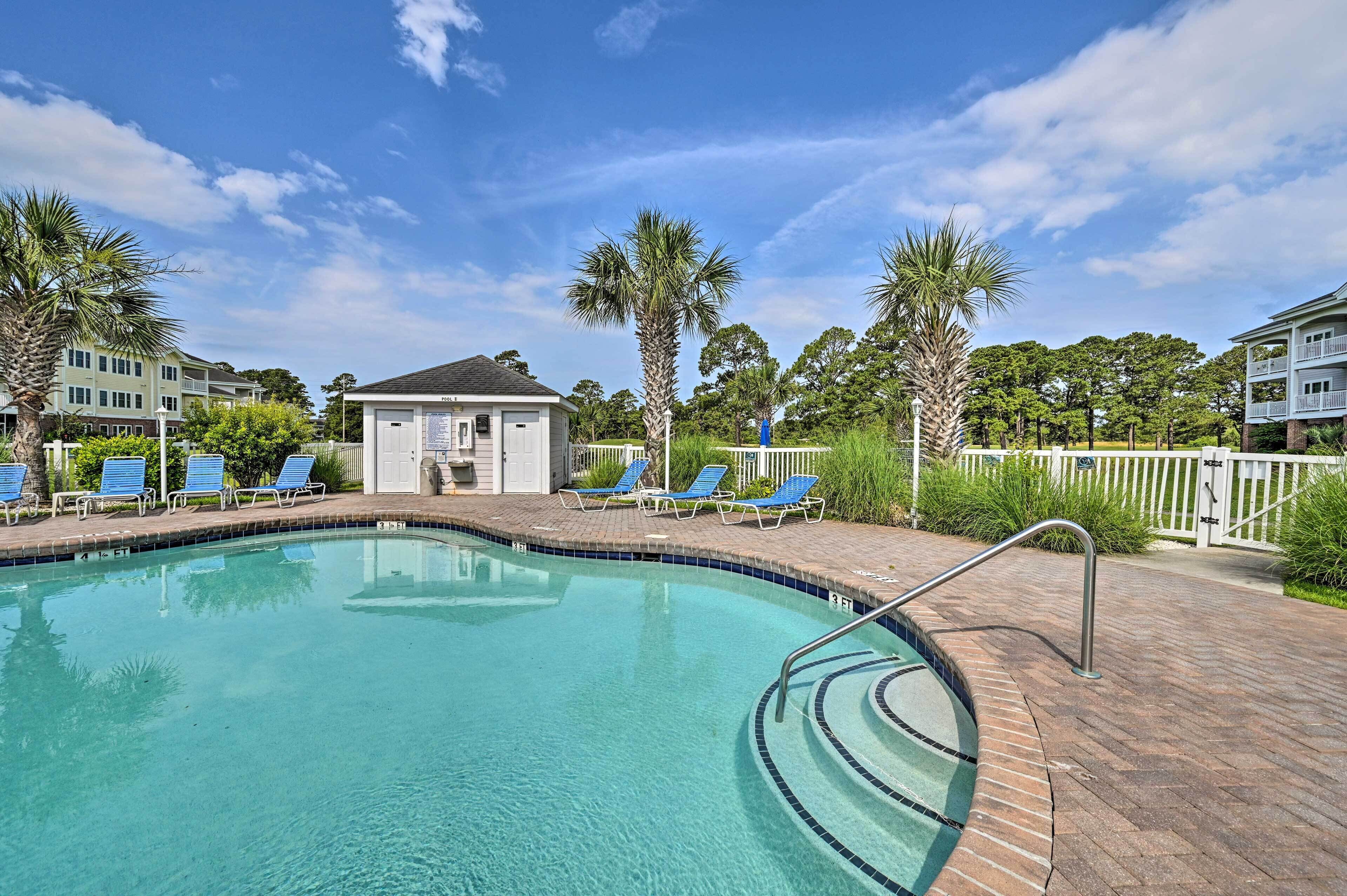 A swimming pool with blue lounge chairs, a small building, and palm trees.