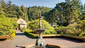 A fountain in a landscaped garden with a house in the background. - Fishermen's Paradise in Coos Bay: Walk to Beach! (Coos Bay)