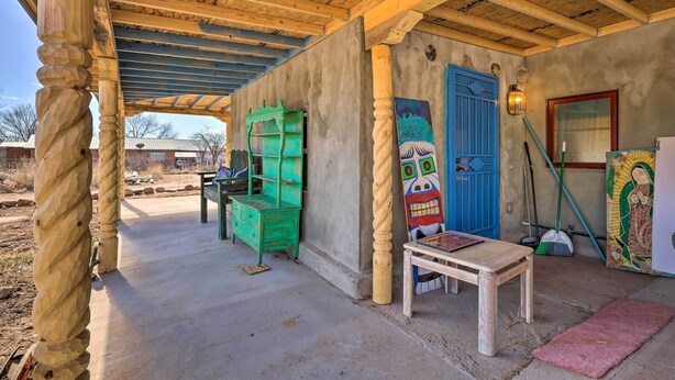 A covered outdoor area with a concrete floor, wooden beams, a green bench, a table, and a blue door. - Santa Cruz Home w/ Mountain Views! (Santa Cruz)