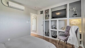 Un dormitorio moderno con cama, televisor integrado, estanterías y una silla.