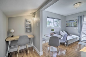 A modern room with a wooden desk, two grey chairs, a round table, a grey sofa, and a window with a view of trees.