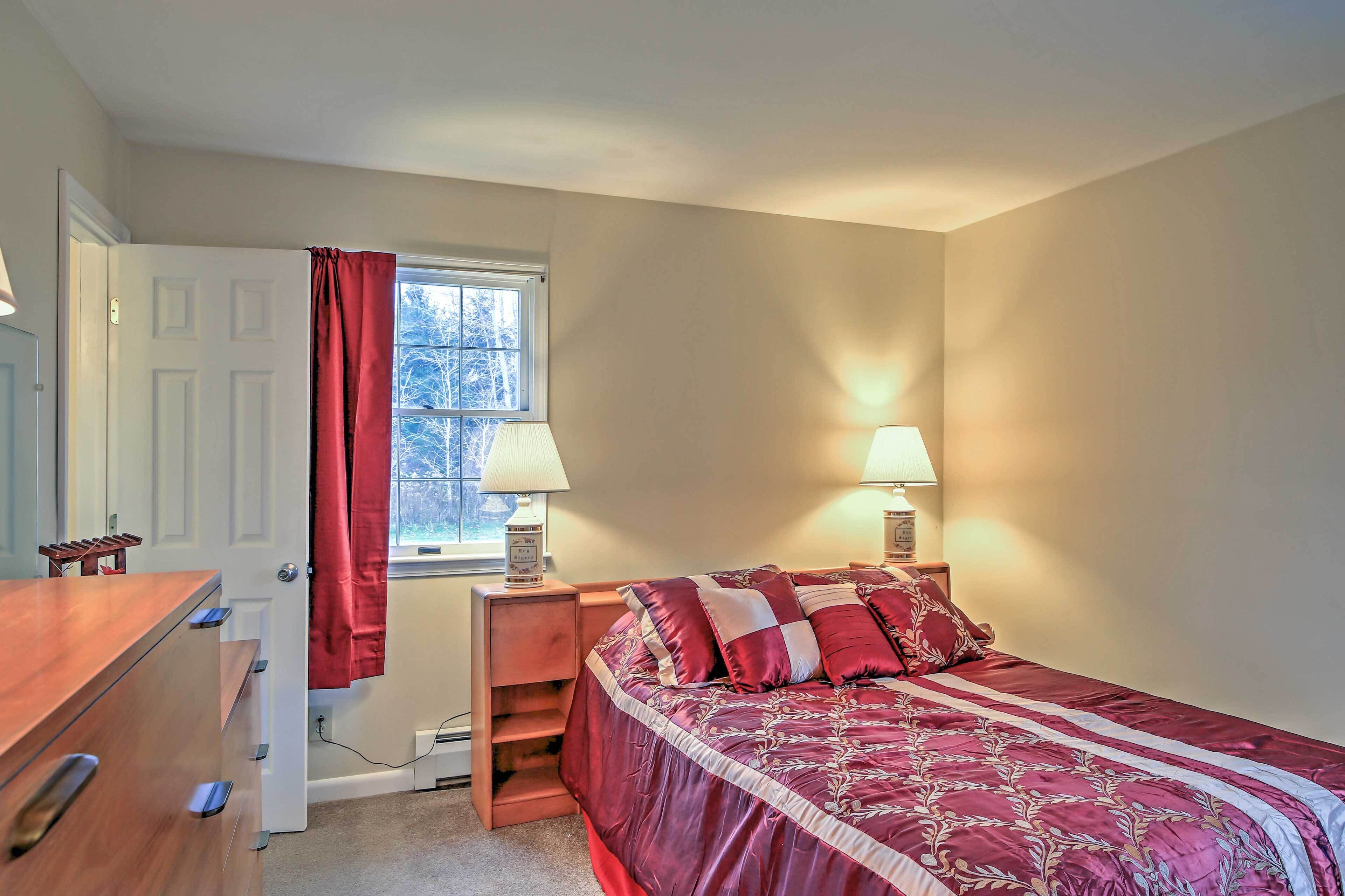 A bedroom with a bed, a desk, a chair, a window with curtains, and two bedside lamps.