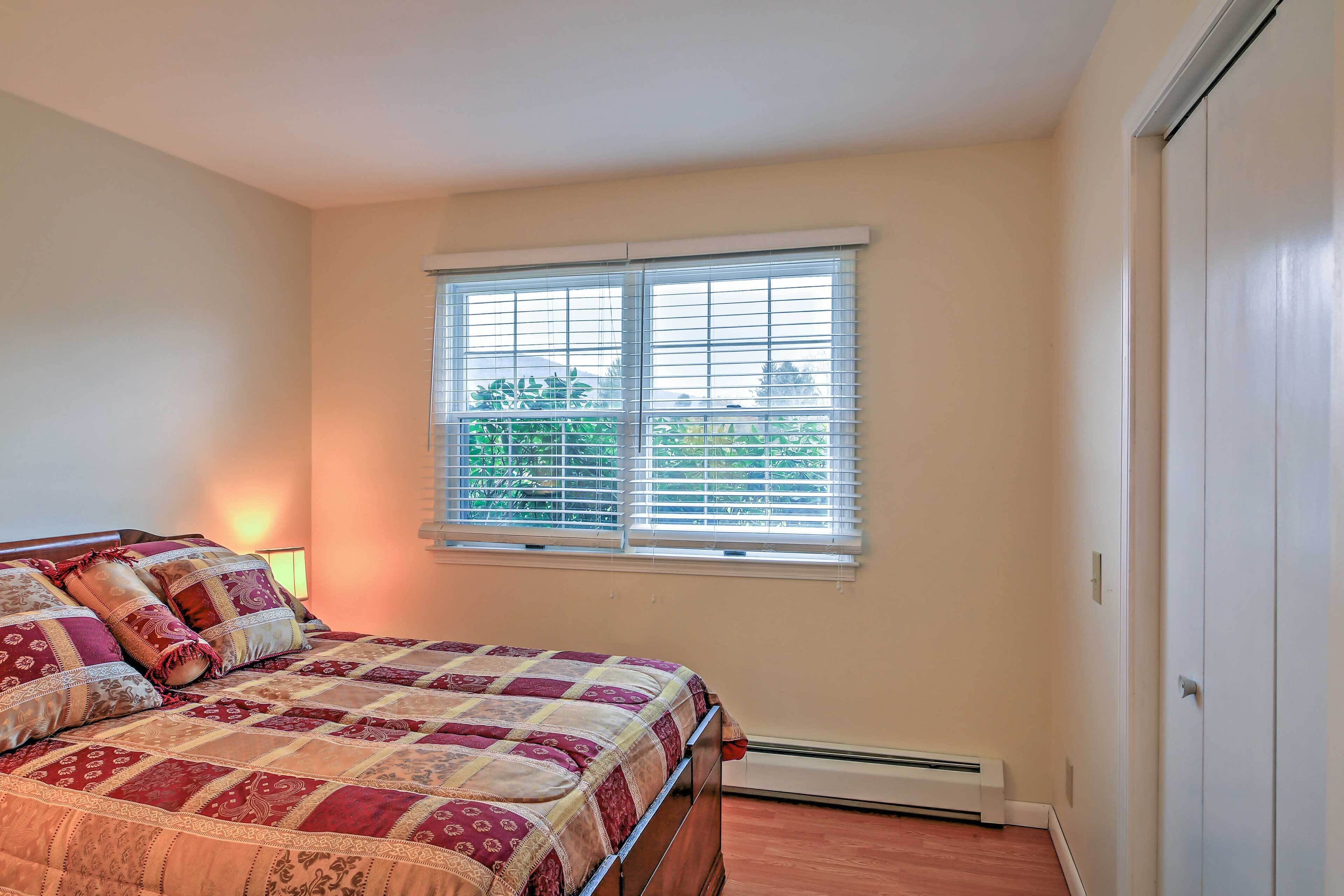 A bedroom with a bed, a window with blinds, a heater, and a door.