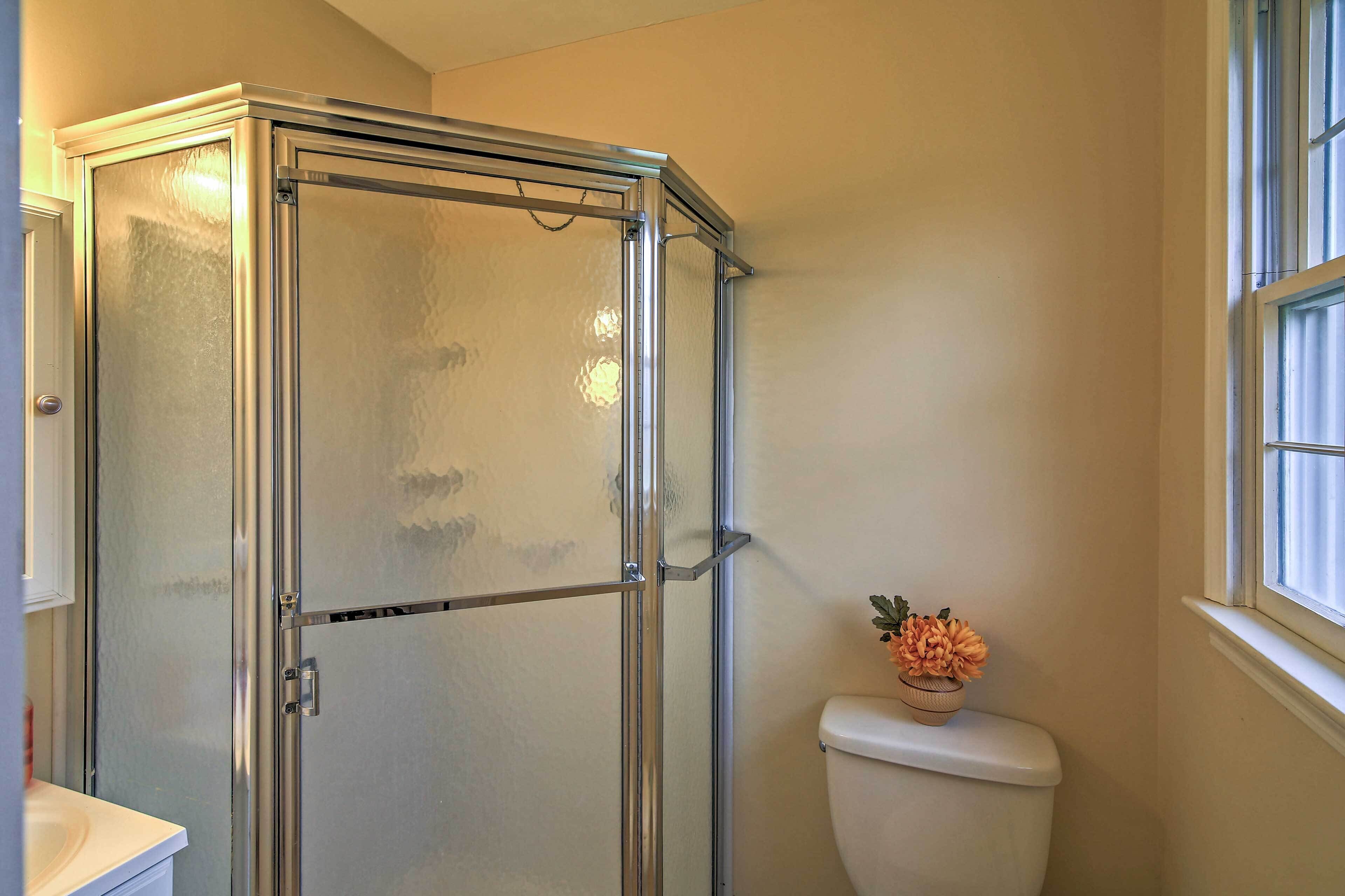 A bathroom with a glass shower enclosure, a toilet, and a window.
