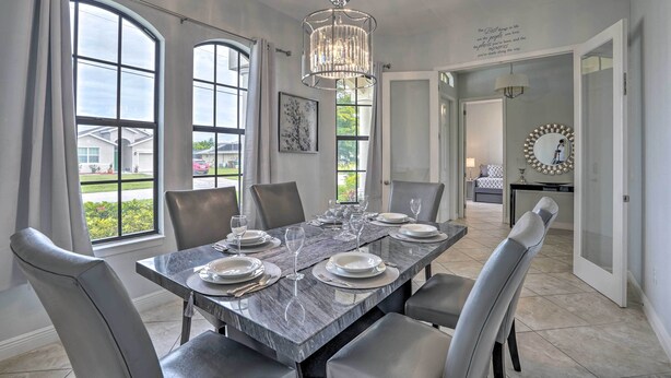 A dining area with a marble table set for six, large windows, and a chandelier. - Private Hot Tub: Canal-front Home in Cape Coral! (Cape Coral)