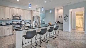 A modern kitchen with white cabinets, a central island with bar stools, stainless steel appliances, and pendant lighting. - Private Hot Tub: Canal-front Home in Cape Coral! (Cape Coral)