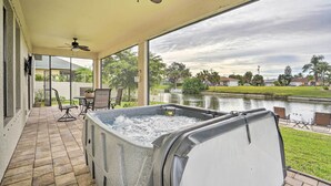 A covered patio with a hot tub, outdoor seating, and a view of a lake. - Private Hot Tub: Canal-front Home in Cape Coral! (Cape Coral)