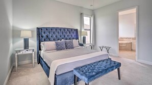 A bedroom with a large bed, a ceiling fan, a nightstand with a lamp, and a view into the bathroom. - Private Hot Tub: Canal-front Home in Cape Coral! (Cape Coral)
