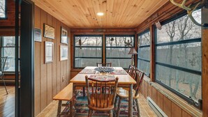 Une salle à manger aux murs lambrés, avec une grande table, des chaises et une vue sur l’extérieur grâce à de grandes fenêtres.