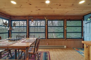 A wooden interior with a dining table, chairs, and large windows offering a view of trees. - Secluded Cresco Cabin w/ Deck + Forest Views! (Cresco)