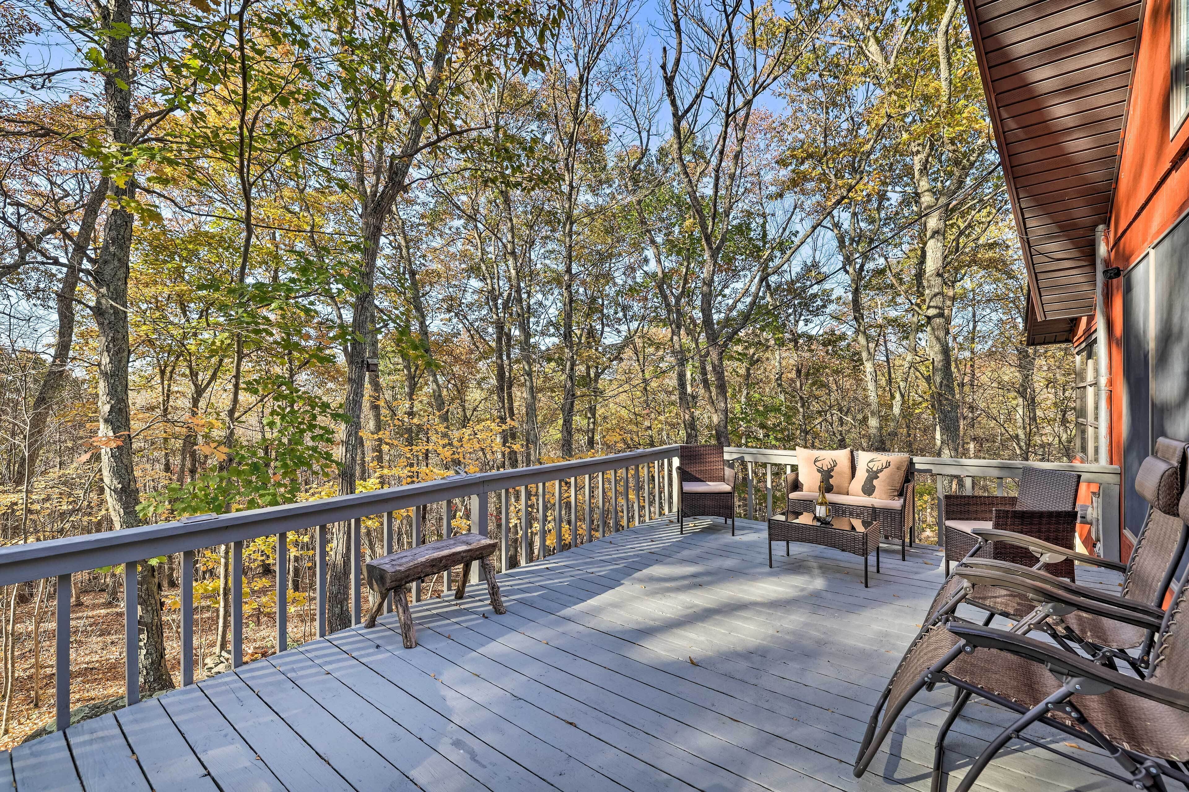 A wooden deck with outdoor furniture, surrounded by trees with autumn foliage.