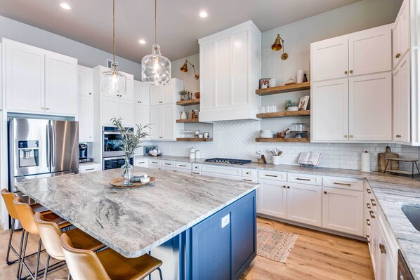Una cocina moderna con armarios blancos, una isla de mármol y electrodomésticos de acero inoxidable.