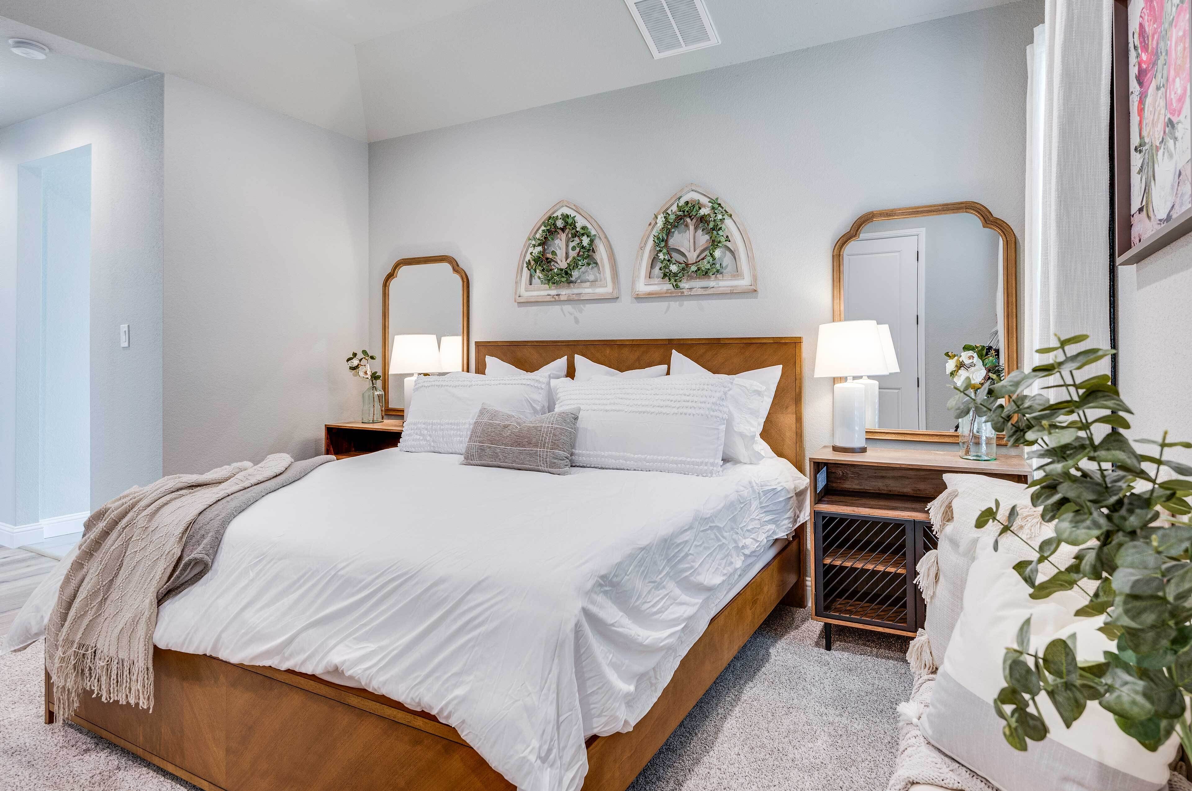 Un dormitorio con cama de madera, ropa de cama blanca, dos mesitas de noche con lámparas y un espejo.