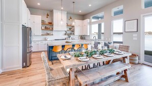 Una cocina moderna con armarios blancos, una isla central y una zona de comedor con mesa y sillas de madera.