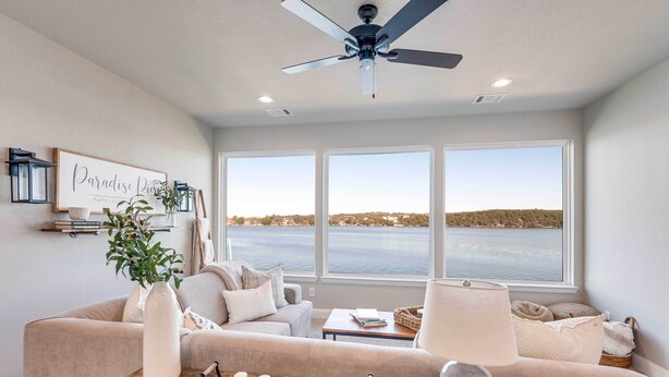 Sala de estar con un amplio ventanal, ventilador de techo y vista a una masa de agua.