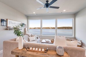 Sala de estar con un amplio ventanal, ventilador de techo y vista a una masa de agua.