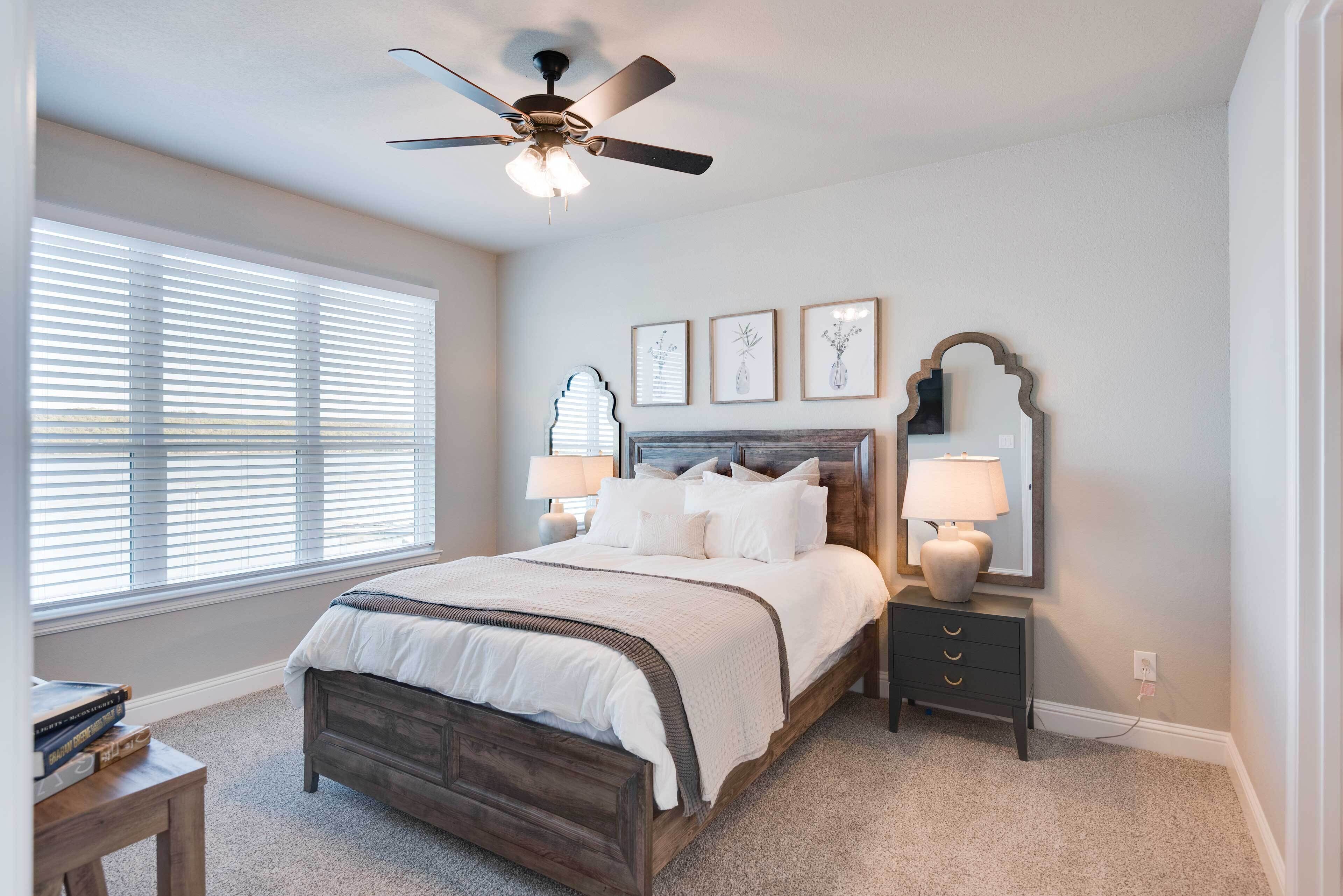A bedroom with a bed, bedside tables, a ceiling fan, and framed artwork on the wall.