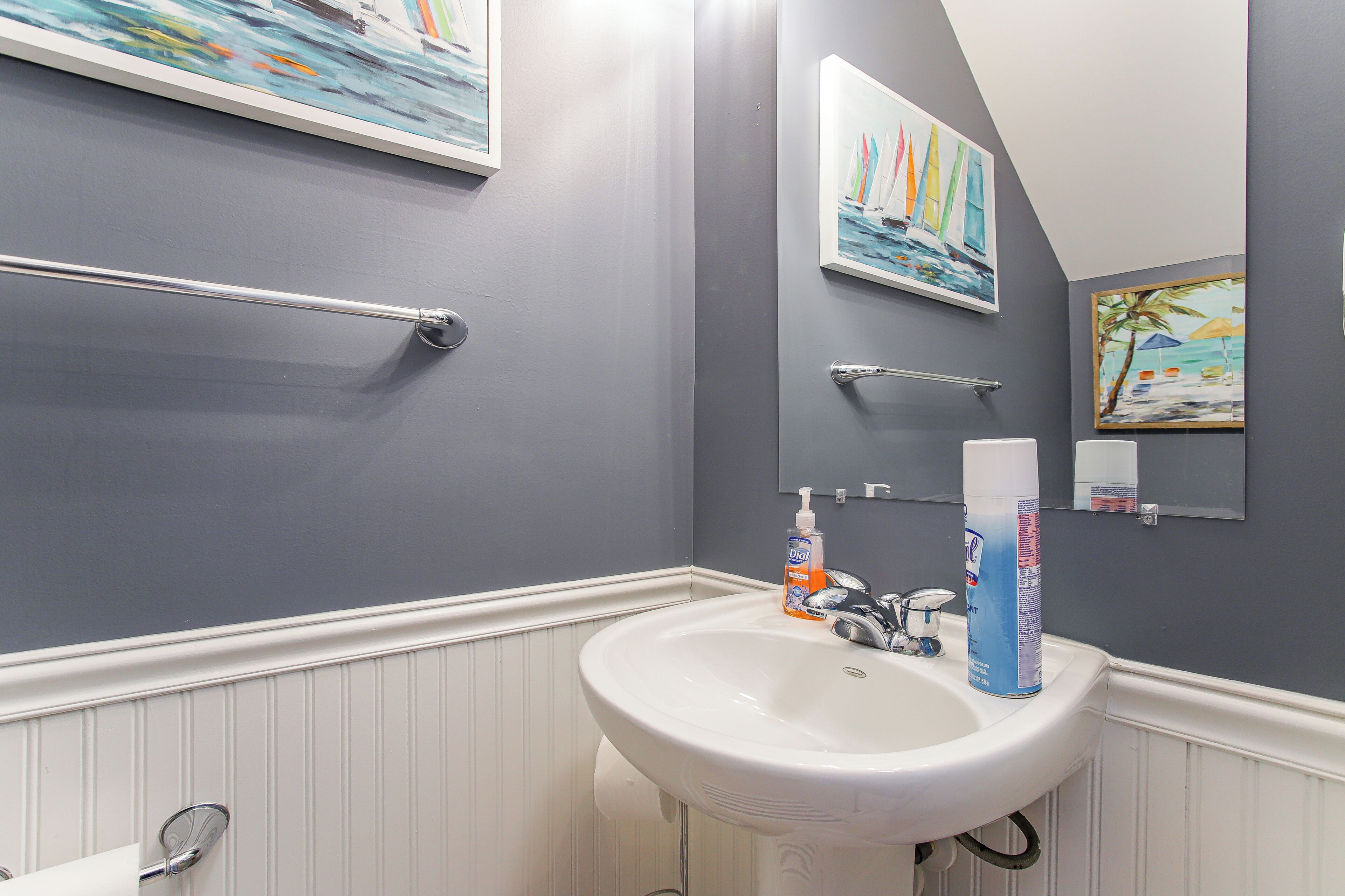 A bathroom with a white sink, a towel rack, and two framed paintings on the wall.