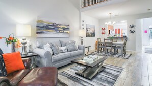 A spacious living room with a grey sofa, a coffee table, and a dining area with a wooden table and chairs. - 3 Mi to Boardwalk: Bethany Beach House w/ Patio! (Ocean View)