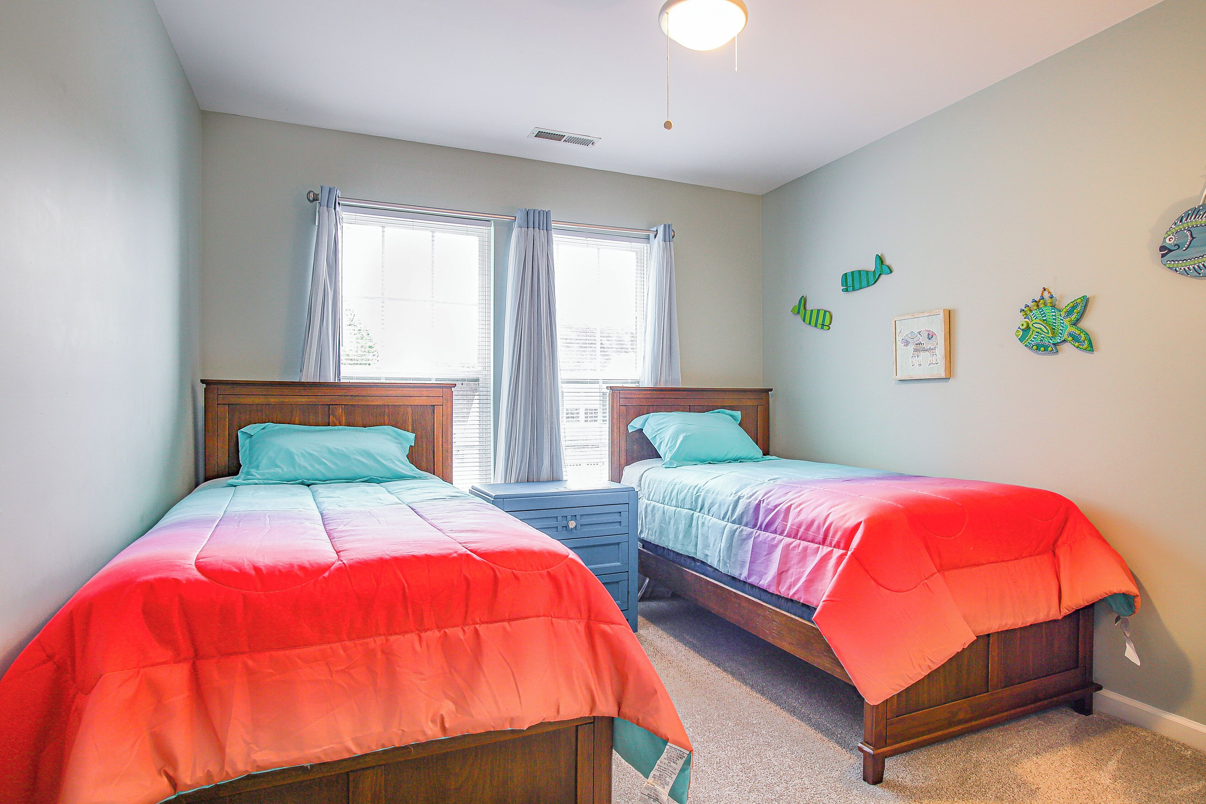 A bedroom with two beds, a nightstand, and a window with curtains.