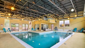 Una piscina interior con agua cristalina, rodeada de sillas azules y un techo alto con vigas a la vista.