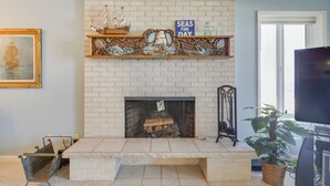 Una sala de estar con chimenea de ladrillo blanco, una estantería con motivos náuticos y un televisor.