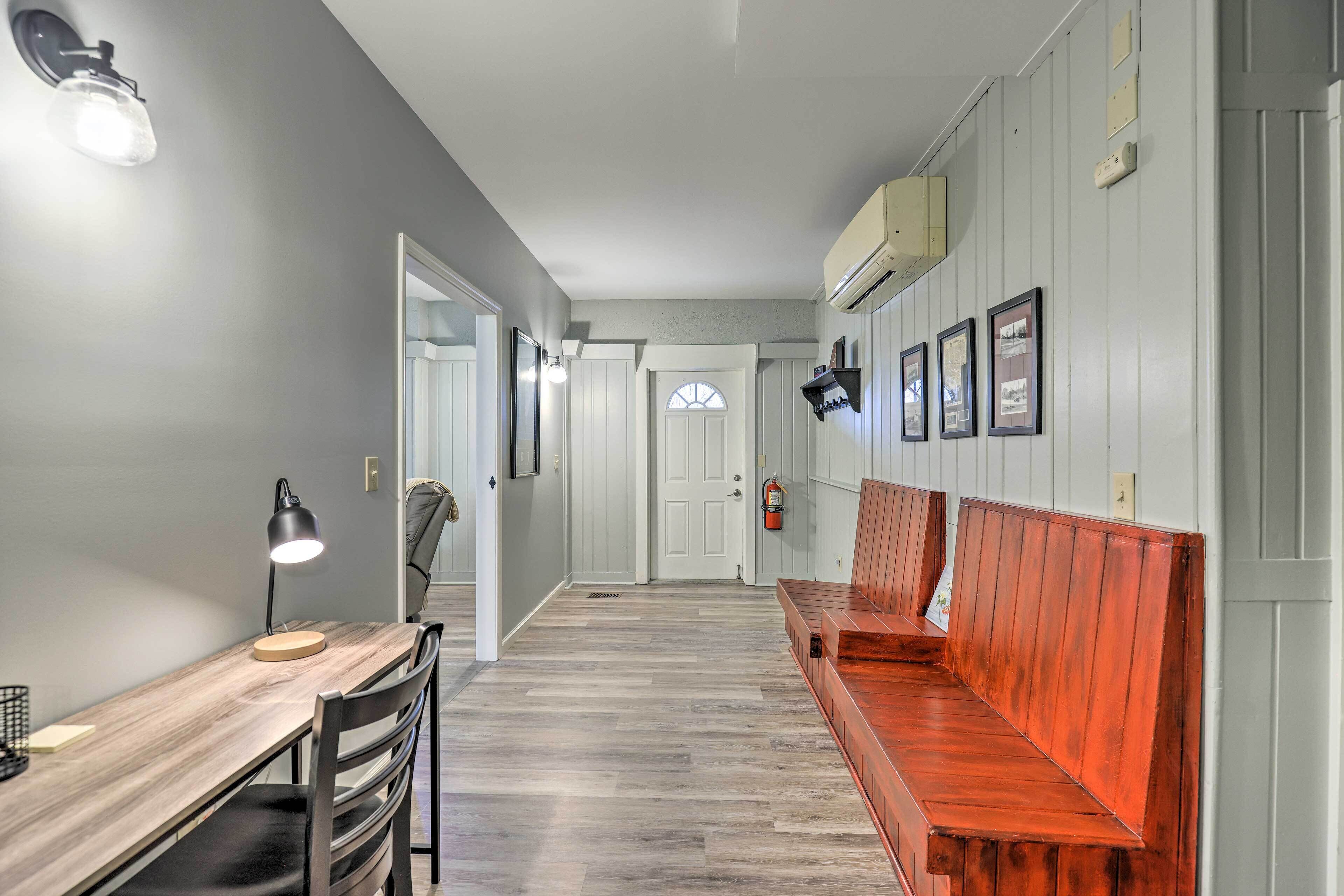 Un couloir avec un banc en bois, un bureau avec une lampe et des tableaux encadrés accrochés au mur.