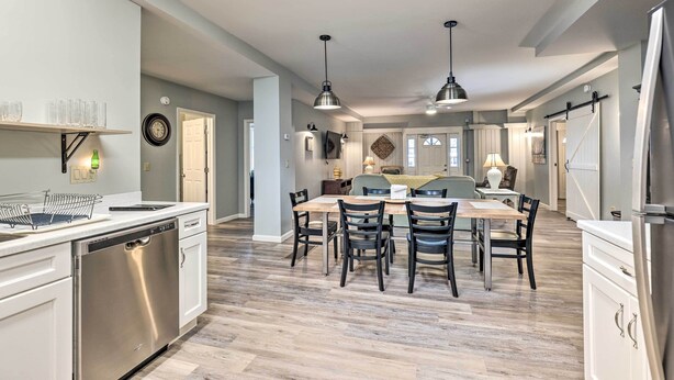 A modern kitchen with a dishwasher, a dining table with chairs, pendant lights, and a refrigerator. - Himrod Vacation Rental 3 Mi to Seneca Lake! (Himrod)