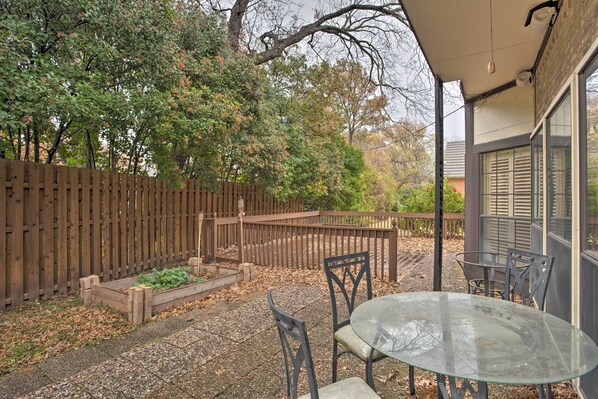 A patio with a glass table and chairs, surrounded by a wooden fence and trees.