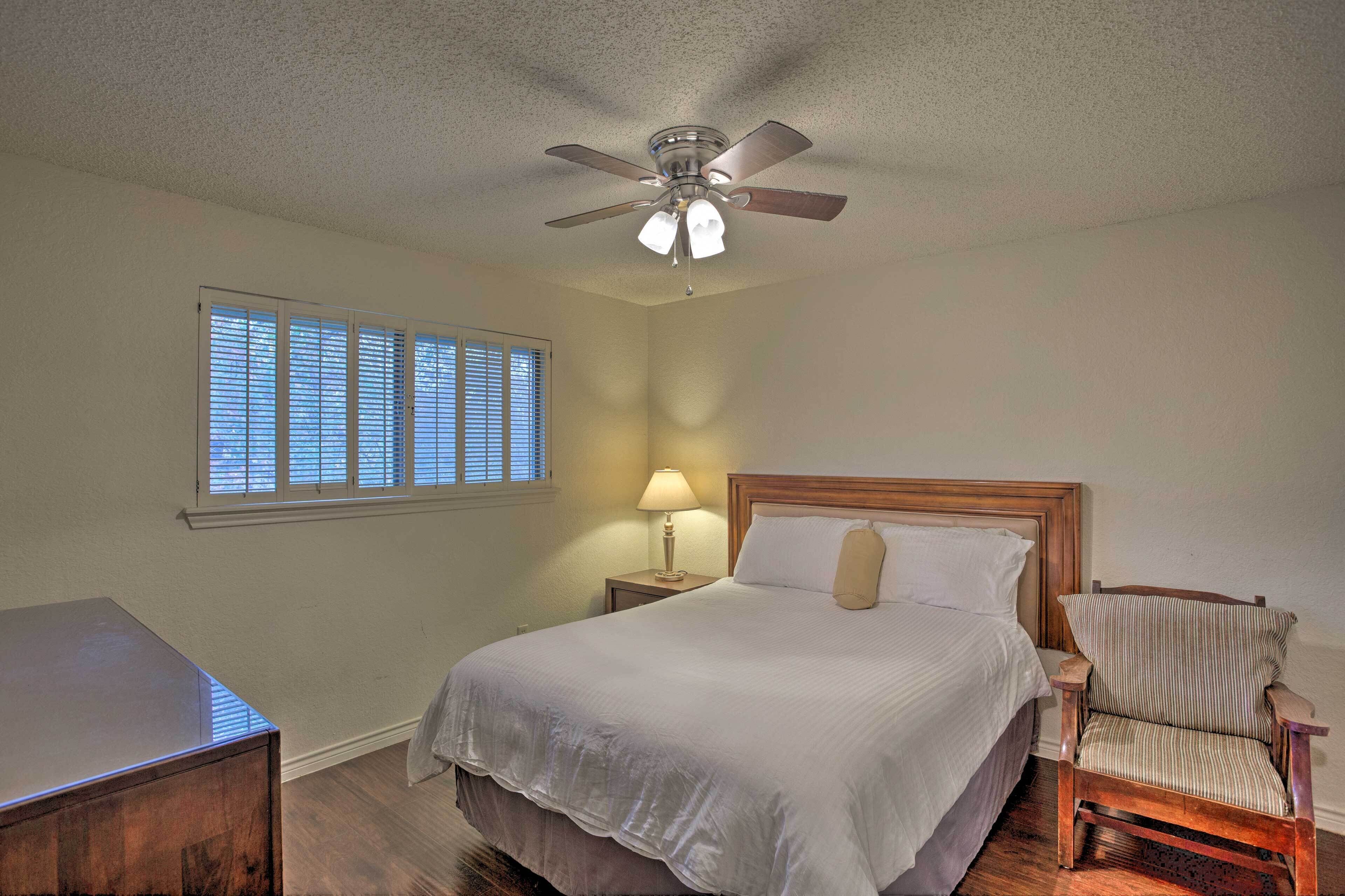 A bedroom with a bed, a chair, a nightstand, a ceiling fan, and a window with blinds.
