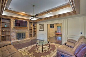 A spacious living room with a fireplace, leather sofas, a glass coffee table, and a ceiling fan.