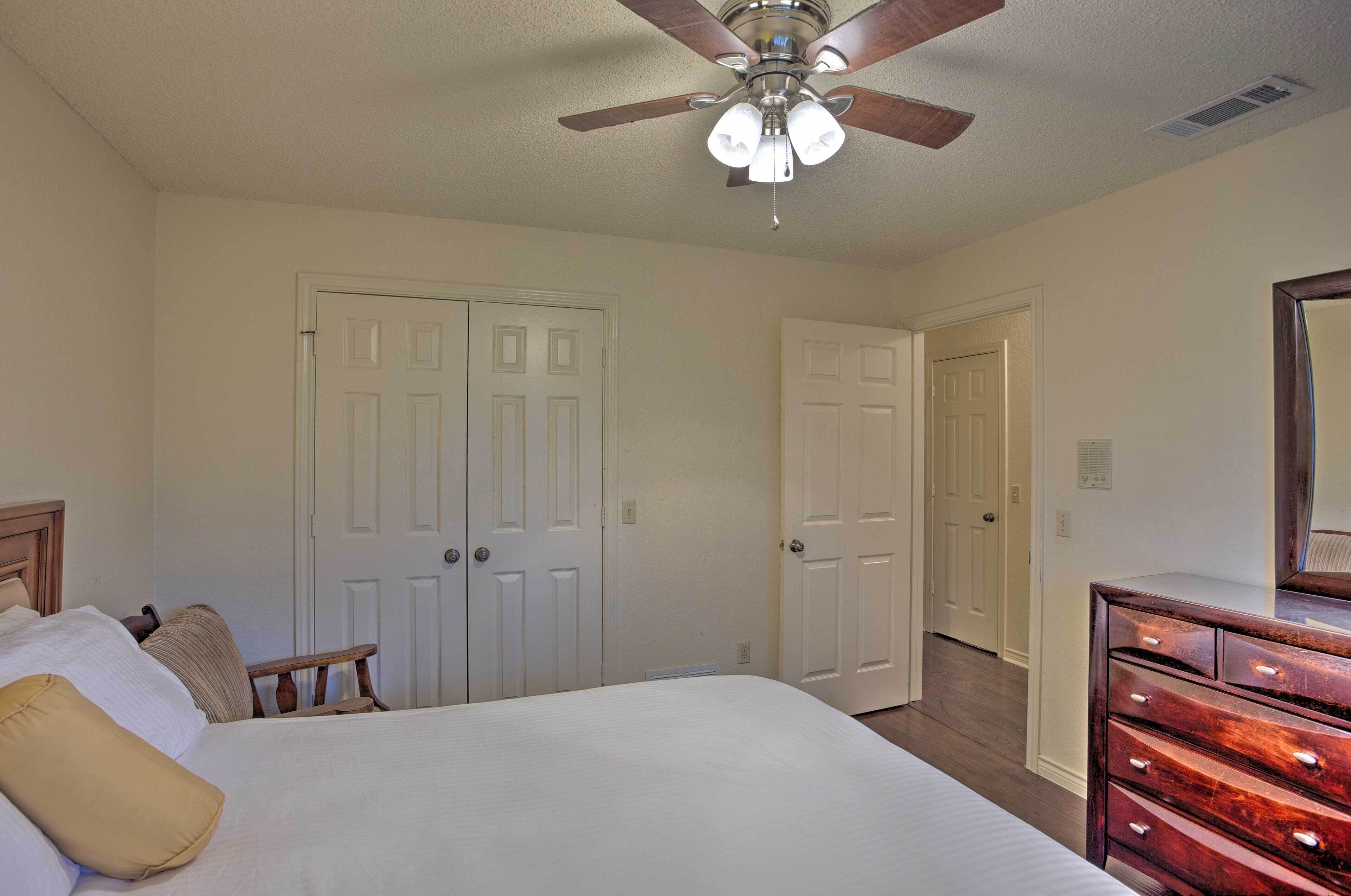 A bedroom with a bed, a dresser, a ceiling fan, and two doors.