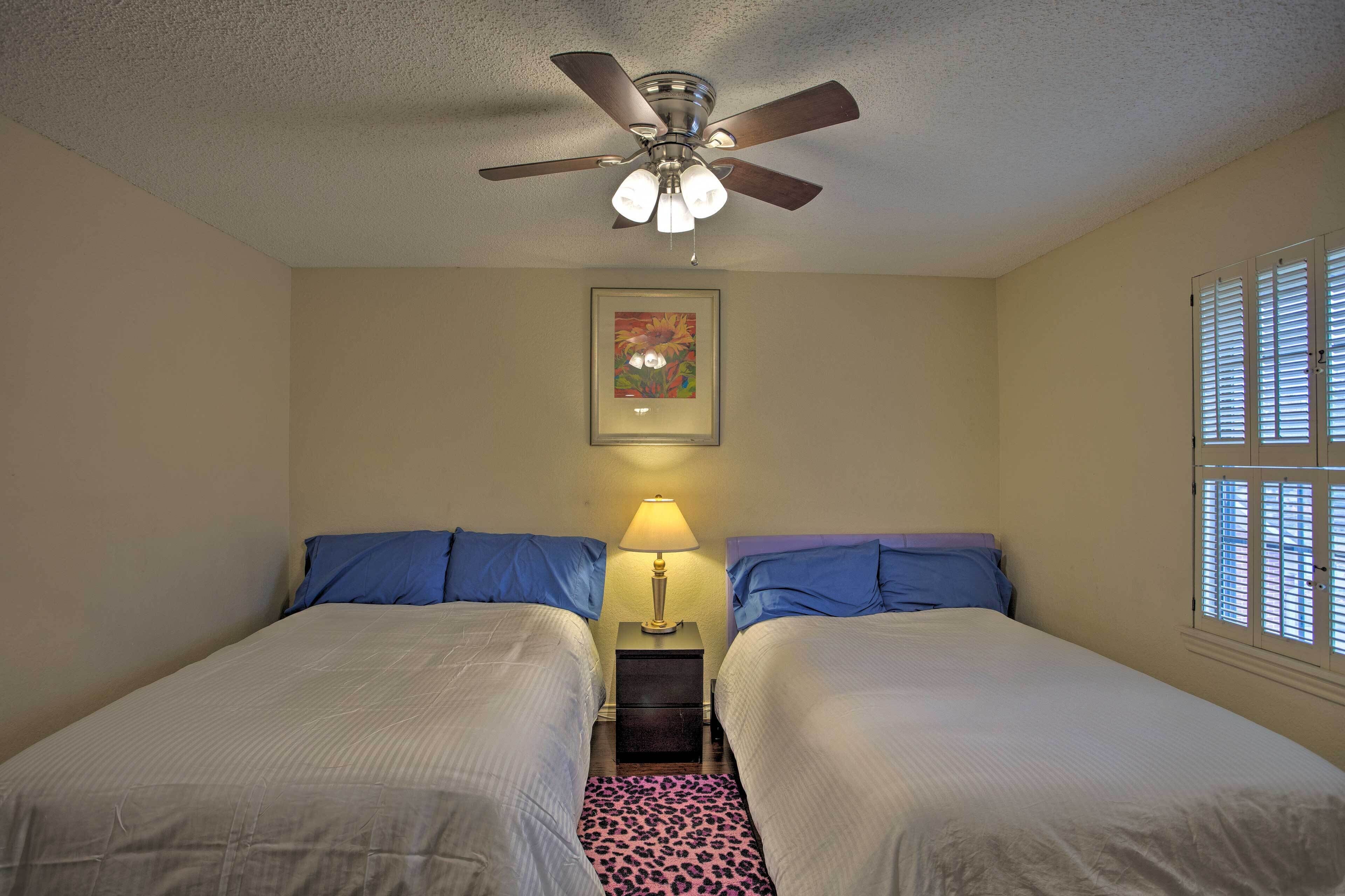 A bedroom with two beds, a ceiling fan, a nightstand with a lamp, and a framed picture on the wall.