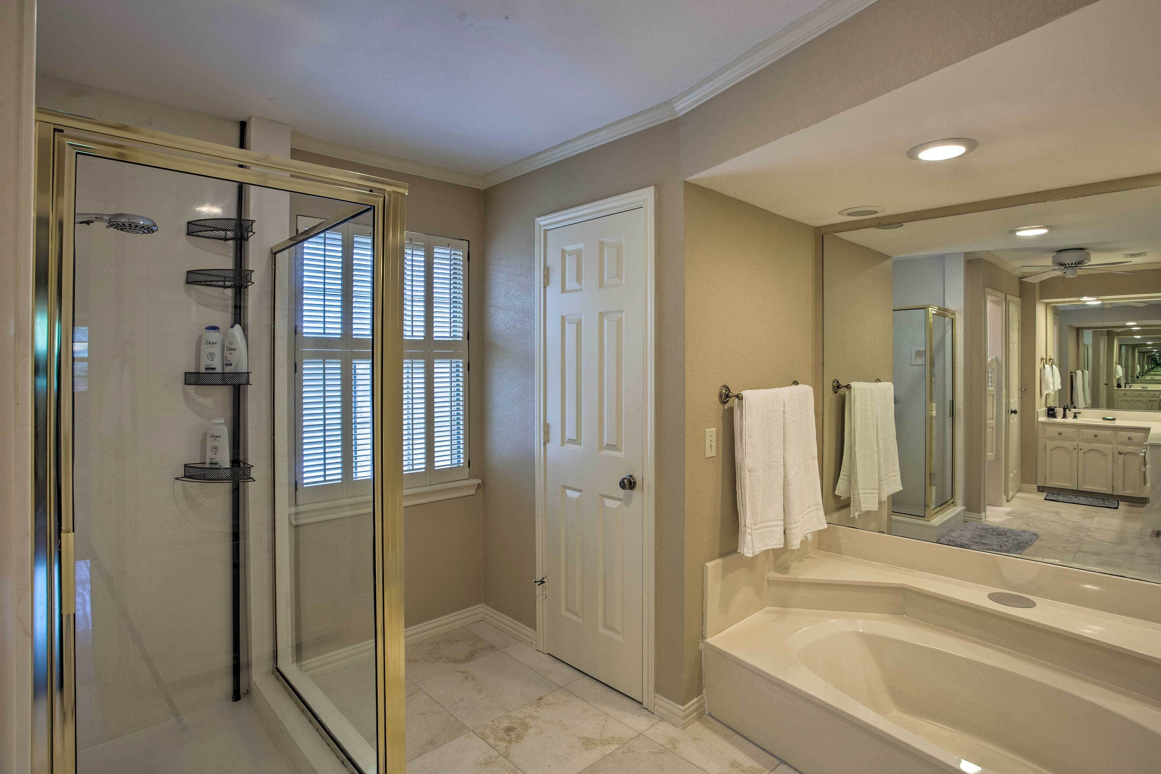 A bathroom with a glass shower enclosure, a white bathtub, and a large mirror reflecting the room.