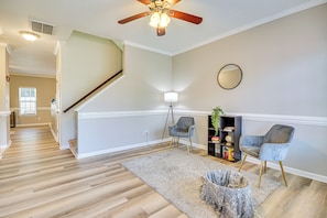A spacious living room with a wooden floor, a ceiling fan, a staircase, and a bookshelf.
