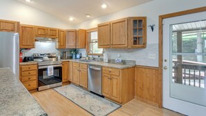 A kitchen with wooden cabinets, stainless steel appliances, a granite countertop, and a glass door leading outside. - Pet-friendly Waynesville Retreat w/ Hot Tub! (Waynesville)