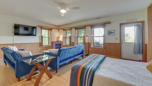 A spacious living area with a large bed, two blue sofas, a glass coffee table, and a flat-screen TV mounted on the wall. - Pet-friendly Waynesville Retreat w/ Hot Tub! (Waynesville)